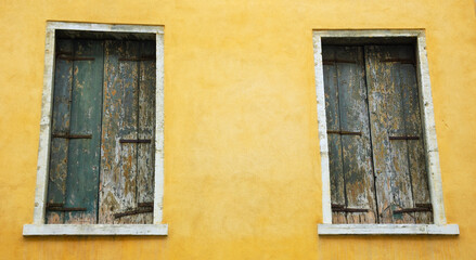 Fototapeta na wymiar Abandoned palazzo in Venice, Italy. Ocher yellow stucco wall and closed wooden shutters with peeling paint.