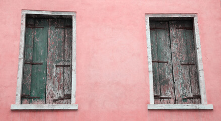 Fototapeta na wymiar Abandoned palazzo in Venice, Italy. Pink stucco wall and closed wooden shutters with peeling paint.