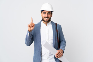 Young architect man with helmet and holding blueprints isolated on white background pointing up a great idea