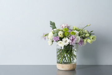 Bouquet with beautiful Eustoma flowers in vase on grey table against light background. Space for text