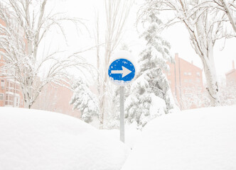 A road sign One Way Arrow Right stands on a snow-covered city street.