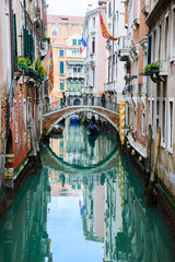 Fototapeta na wymiar Venice gondola tour. Canal scene. Tourists enjoying gondola ride during Carnival. Flags over houses - Venetian, French. Venice, Italy