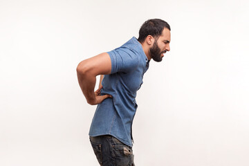 Side view exhausted unhealthy bearded man touching aching back, suffering lower lumbar discomfort,...