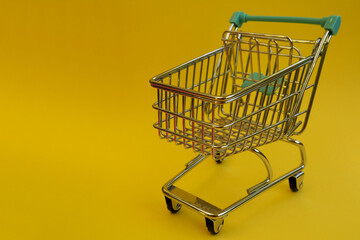 close up is a small metal trolley with blue handles from a supermarket on a yellow background side view . sales through an online store