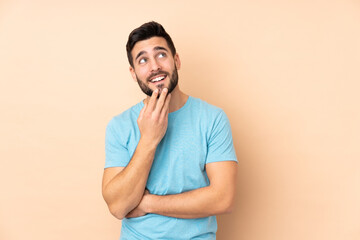Caucasian handsome man isolated on beige background looking up while smiling