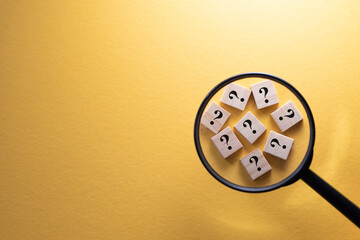 Focus on Question Mark symbol on a wooden tiles using magnifying glass against yellow background....