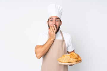 Male baker holding a table with several breads isolated on white background with surprise facial expression
