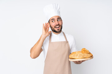 Male baker holding a table with several breads isolated on white background listening something