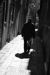 Silhouette of  old man going on narrow street in shining sun rays. Venice, Italy. A game of light and shadow. Black white historic photo.