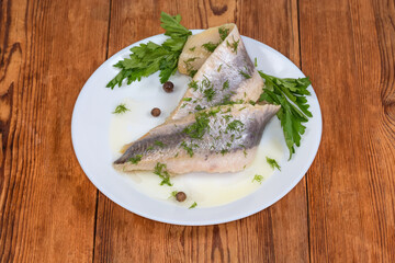 Pickled herring fillets on dish with parsley on rustic table