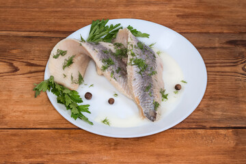 Pickled herring fillets with greens on dish on rustic table