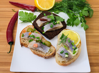 Different open sandwiches with pickled herring on square dish