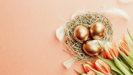 Obraz na płótnie Canvas Easter Golden eggs in basket with spring tulips, white feathers on pastel pink background in Happy Easter decoration. Spring holiday flat lay concept.