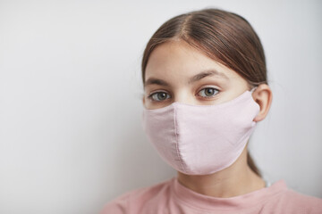 Close up portrait of cute girl wearing pink mask and looking at camera while standing against white background, copy space
