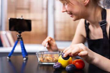 Obraz na płótnie Canvas An enlarged photo of a food blogger girl in front of the phone camera with cereals and fruits on a blurred background. The concept of stream blogging and proper nutrition.
