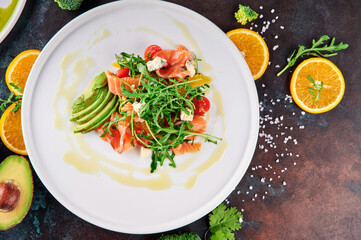 Salad with arugula, salmon, avocado, cherry tomatoes and feta cheese on a white plate. Oxidized background. close-up