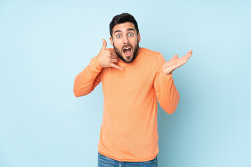 Fototapeta premium Caucasian handsome man making phone gesture and doubting over isolated blue background