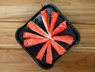 fresh raw crab stick sliced on square plate isolated on wooden background, shabu, hot pot ingredients