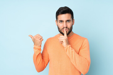 Caucasian handsome man pointing to the side and doing silence gesture over isolated blue background