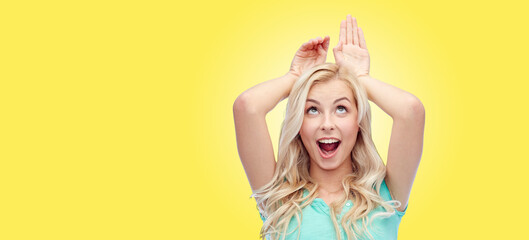 fun, expressions, easter and people concept - happy smiling young woman making bunny ears over...