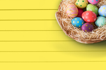 easter, holidays, tradition and object concept - close up of colored eggs in wicker basket over yellow wooden boards background
