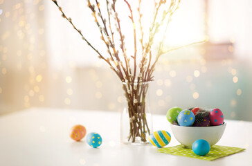 holidays and object concept - pussy willow branches and colored easter eggs in vase on table over bokeh lighs