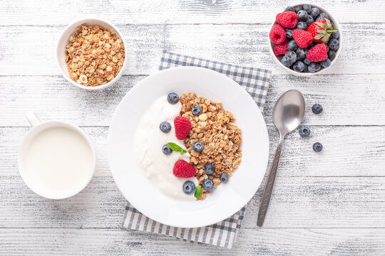Yogurt with baked granola and berries in white ceramic plate on wooden background. Healthy breakfast. Copy space - Image