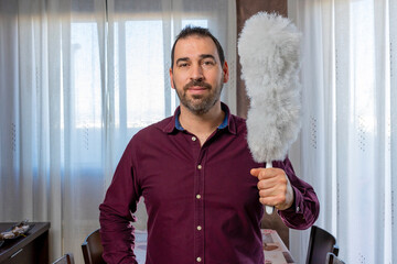 Bearded man in a purple shirt posing funny with a cleaning duster