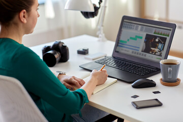 technology, post production and vlog concept - close up of woman working in video editor program on laptop computer writing to notebook at home office