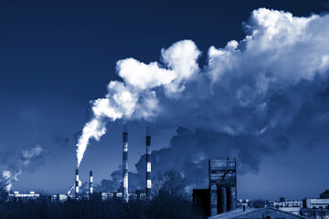 Air polluting pipes of the factory, big clouds of smoke. A horizontal photograph toned in classic blue