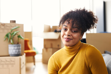 Portrait Of Young Woman Sitting On Floor And Smiling As She Moves Into New Home Surrounded By Boxes
