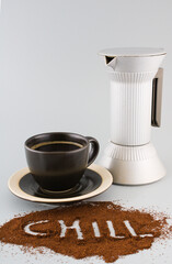 Cup of black coffee on a saucer, percolator and sign saying chill written in ground coffee beans isolated on neutral background