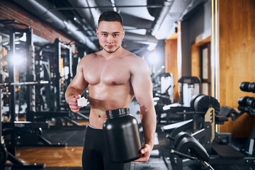 Fototapeta na wymiar Smiling young bodybuilder taking supplements in gym