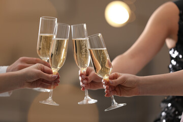 People clinking glasses of champagne against blurred background, closeup. Bokeh effect