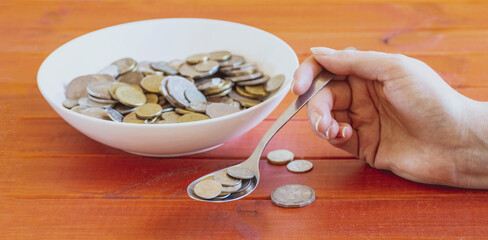hand holding a spoon full of coins next to a bowl with coins. Concept of charity for starving people