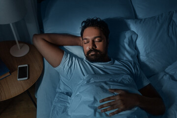 people, bedtime and rest concept - indian man sleeping in bed at home at night