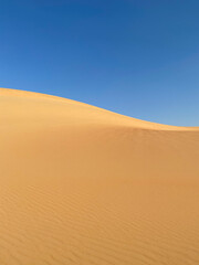 Fototapeta na wymiar Simple abstract desert scenery with sand dunes and blue sky. Liwa desert, Abu Dhabi, UAE.