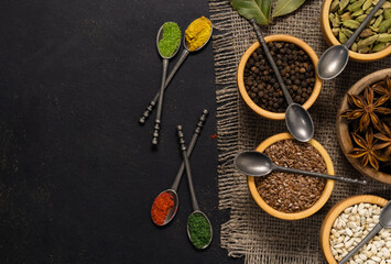 Spices and condiments in spoons and bowls for cooking on black background