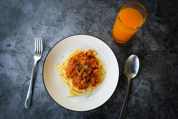 Spaghetti with minced pork tomato sauce on white plate with cutlery and Orange juice.