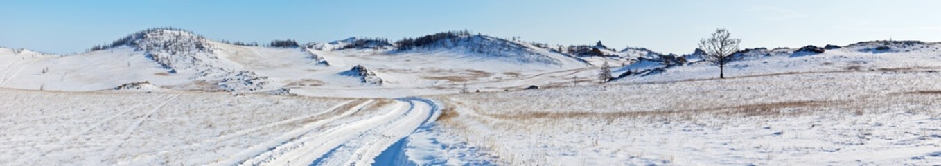 Panoramic view on snowy dirt road on the Tazheran steppe with snow-covered hills. Baikal region, Olkhon district. Winter landscape. Natural wide background, banner. Outdoors and winter travel