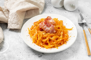 Braised cabbage. Stewed cabbage and bacon in a white plate on the light gray kitchen table. Bigos of cabbage, tomato and bacon. Traditional Polish dish
