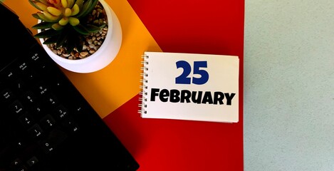 February 25  on a multicolored background on a white notebook.Next to it is an artificial flower in a pot .Calendar for February.
