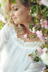 Beautiful young woman with long curly hair and perfect skin posing near blooming roses in the...