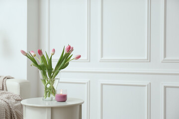 Beautiful tulips and burning candle on white table indoors, space for text. Interior design