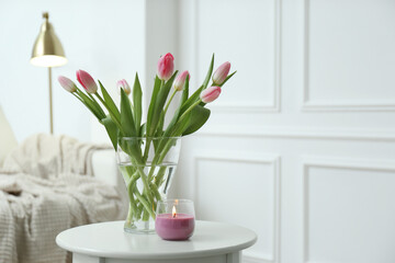 Beautiful tulips and burning candle on white table indoors, space for text. Interior design