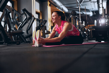 Jolly young woman doing stretching in fitness studio