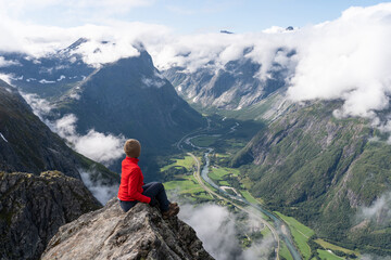 A woman hiker and traveller sitting on rock looking to mountains, Romsdalseggen trekking trail, Norway, Scandinavia