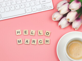 flat lay of wooden letter HELLO MARCH on pink background with coffee cup, computer keyboard and...