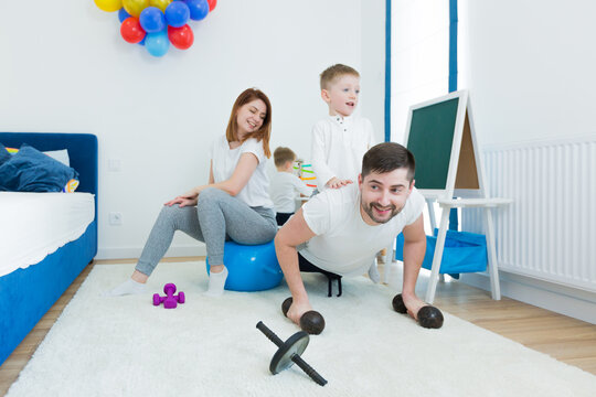 Cheerful family, young man father and young woman mother, doing morning exercise gymnastics with their two young sons. Spend time together in the nursery