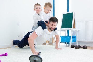 Young man father, doing morning exercise with his two young sons. Spend time together in the nursery